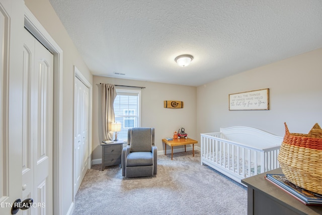 carpeted bedroom featuring two closets, a textured ceiling, and a crib