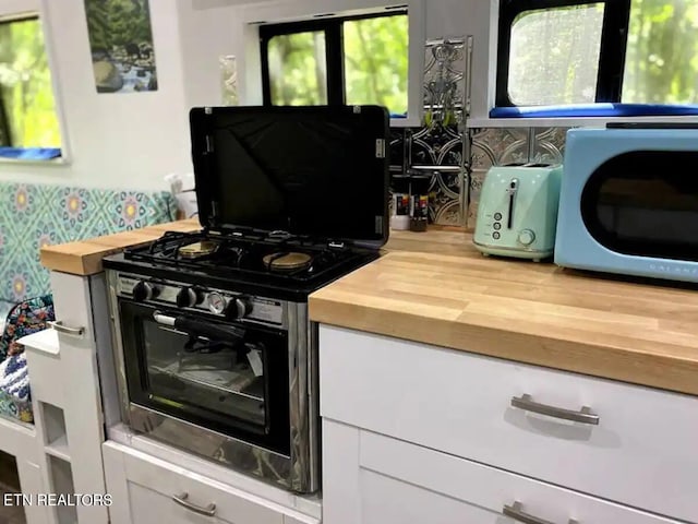 kitchen with butcher block counters, gas stove, and white cabinets