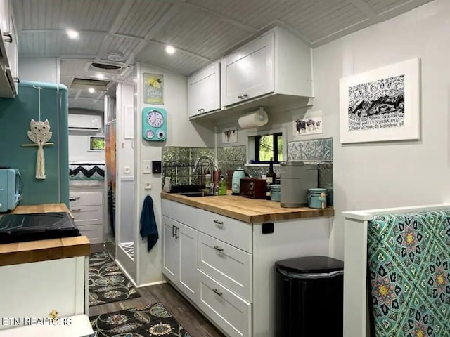 kitchen with sink, wooden counters, dark hardwood / wood-style floors, a wall unit AC, and white cabinets