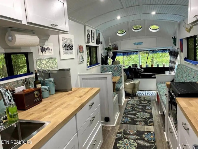 kitchen featuring wood counters, lofted ceiling, sink, dark hardwood / wood-style flooring, and white cabinets