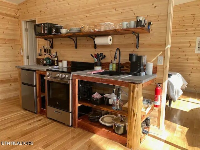 bar featuring wood walls, sink, fridge, electric range, and light wood-type flooring