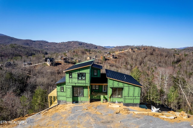 unfinished property with a forest view, a mountain view, and roof mounted solar panels
