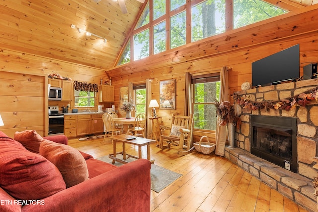 living area with high vaulted ceiling, a stone fireplace, wooden ceiling, wood walls, and light wood finished floors