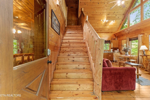 stairway featuring high vaulted ceiling, wooden ceiling, wooden walls, a ceiling fan, and hardwood / wood-style floors