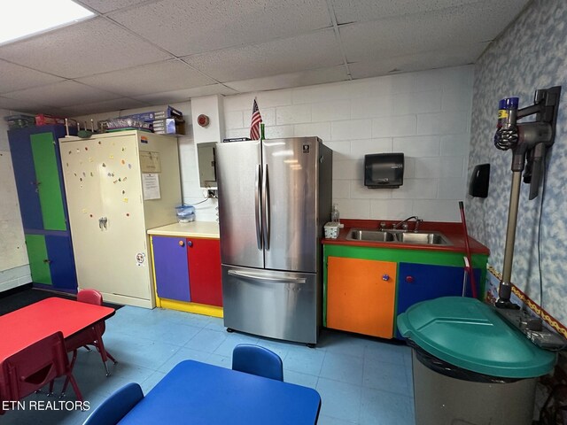 kitchen featuring stainless steel fridge, sink, light tile patterned flooring, and a paneled ceiling