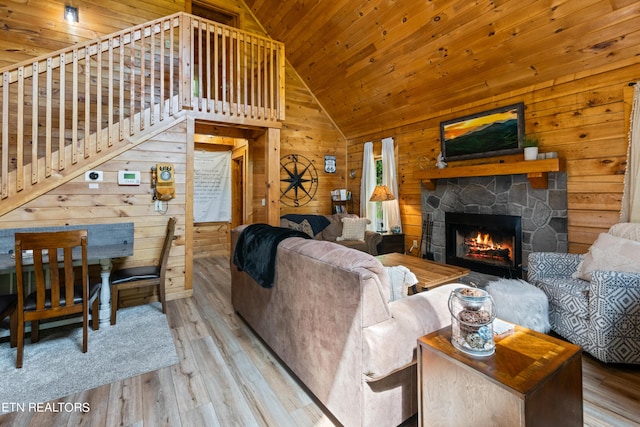 living room with wood ceiling, wood-type flooring, a stone fireplace, wood walls, and high vaulted ceiling