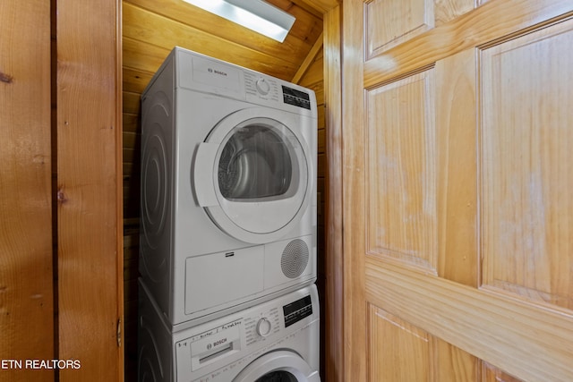 laundry room with stacked washer and clothes dryer and wooden walls