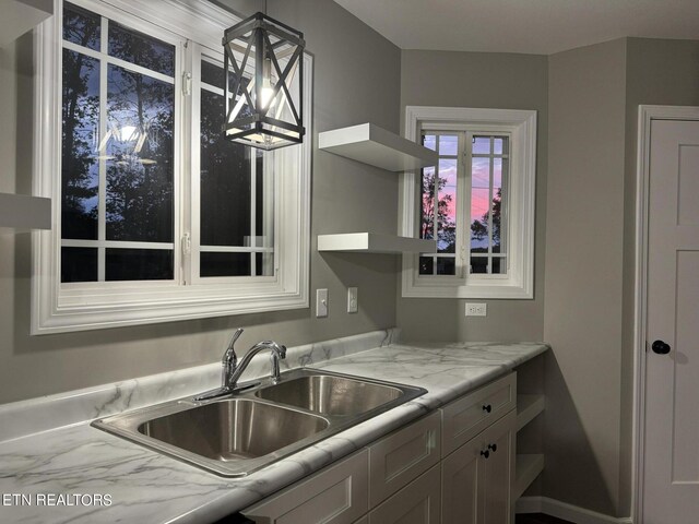 kitchen featuring decorative light fixtures, light stone countertops, and sink