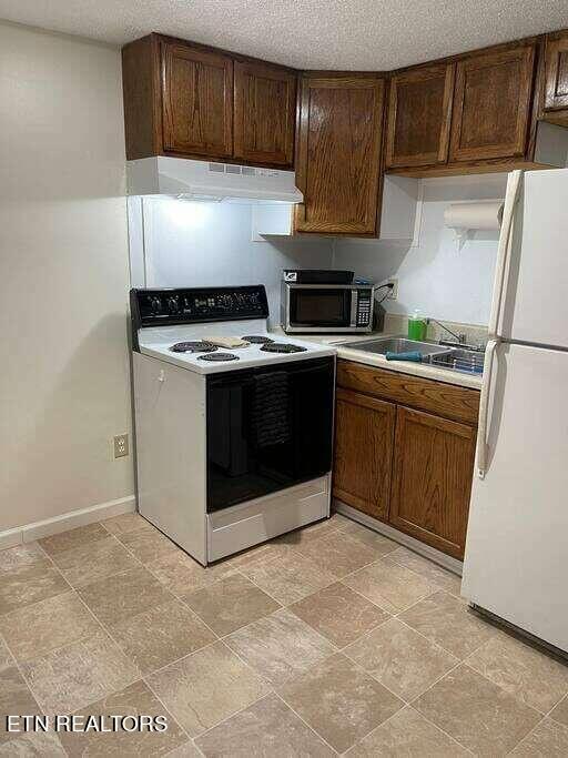 kitchen featuring white appliances, sink, light tile patterned floors, a textured ceiling, and range hood