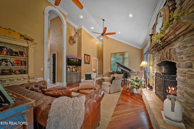 living room with crown molding, ceiling fan, ornate columns, a stone fireplace, and high vaulted ceiling