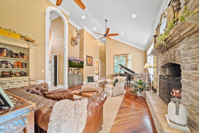 living room with crown molding, decorative columns, ceiling fan, a stone fireplace, and high vaulted ceiling