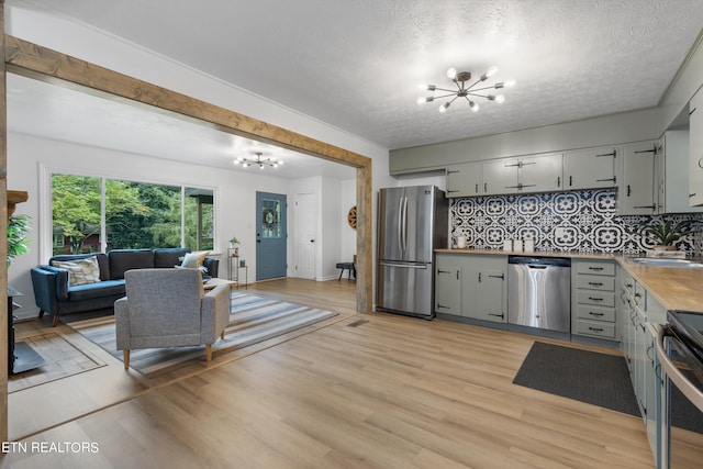 kitchen featuring stainless steel appliances, light hardwood / wood-style floors, backsplash, and a notable chandelier