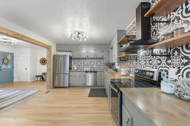 kitchen with appliances with stainless steel finishes, tasteful backsplash, gray cabinetry, light hardwood / wood-style floors, and wall chimney exhaust hood