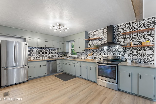 kitchen featuring light hardwood / wood-style flooring, a textured ceiling, stainless steel appliances, wall chimney exhaust hood, and decorative backsplash