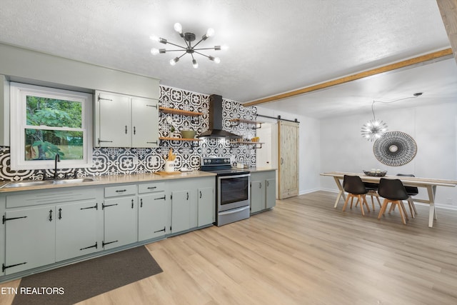 kitchen with electric stove, tasteful backsplash, wall chimney range hood, sink, and a barn door