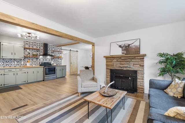 living room featuring a stone fireplace, a barn door, light wood-type flooring, beam ceiling, and a chandelier