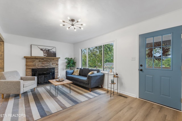 living room featuring a stone fireplace, light hardwood / wood-style flooring, and a notable chandelier