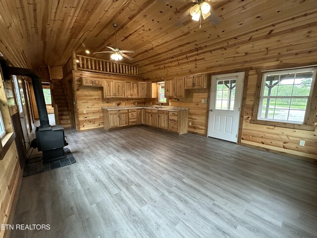 unfurnished living room with a wood stove, wood ceiling, light hardwood / wood-style floors, wood walls, and ceiling fan