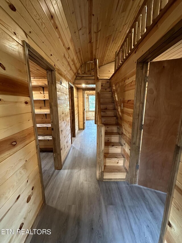 hall with wood ceiling, wooden walls, hardwood / wood-style flooring, and vaulted ceiling