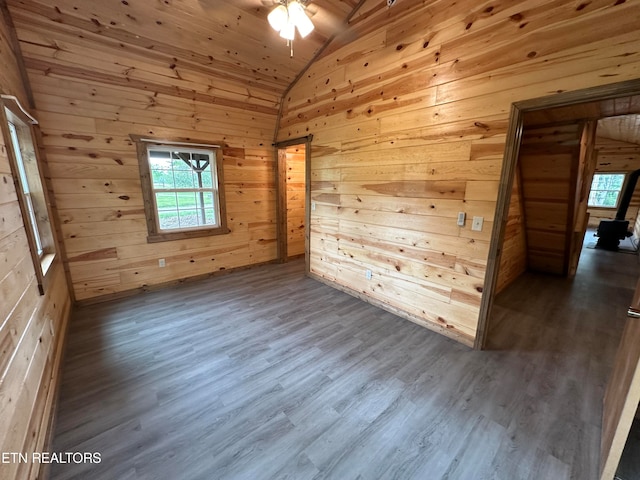 empty room with lofted ceiling, wood walls, ceiling fan, hardwood / wood-style floors, and wooden ceiling