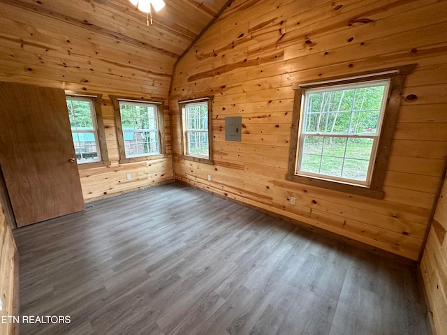 empty room with wooden walls, electric panel, vaulted ceiling, and hardwood / wood-style floors