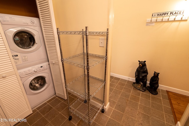 laundry room with stacked washer and dryer and dark tile patterned floors