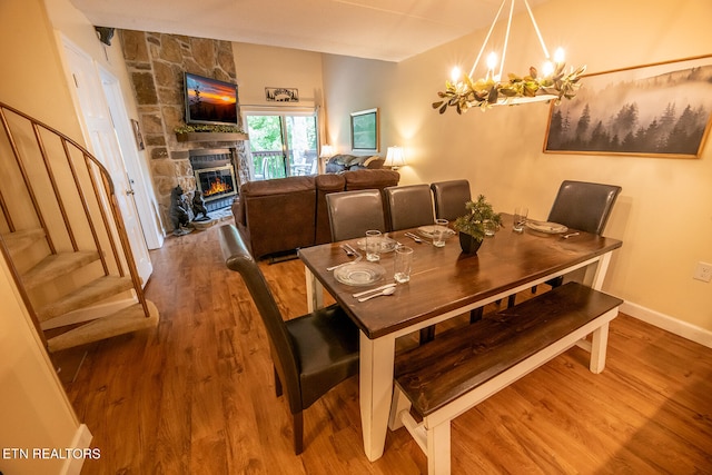 dining area with a stone fireplace, hardwood / wood-style floors, and a chandelier