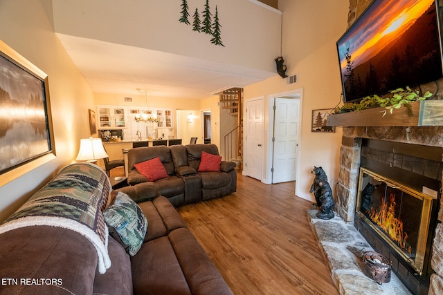 living room featuring a stone fireplace, hardwood / wood-style flooring, and an inviting chandelier