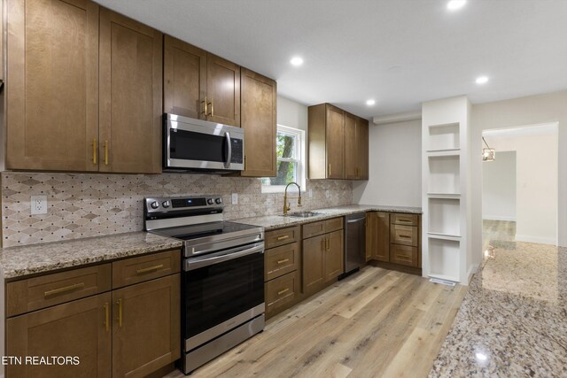 kitchen featuring appliances with stainless steel finishes, light wood-type flooring, backsplash, light stone counters, and sink