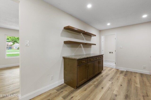 bar featuring dark brown cabinetry, light stone counters, and light hardwood / wood-style flooring