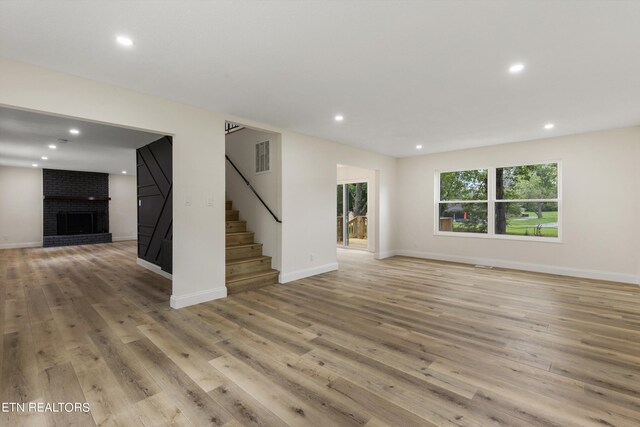 unfurnished living room with light hardwood / wood-style floors and a brick fireplace