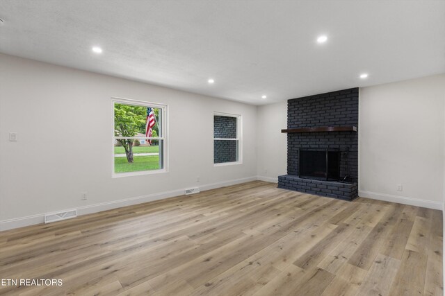 unfurnished living room featuring light hardwood / wood-style floors and a brick fireplace