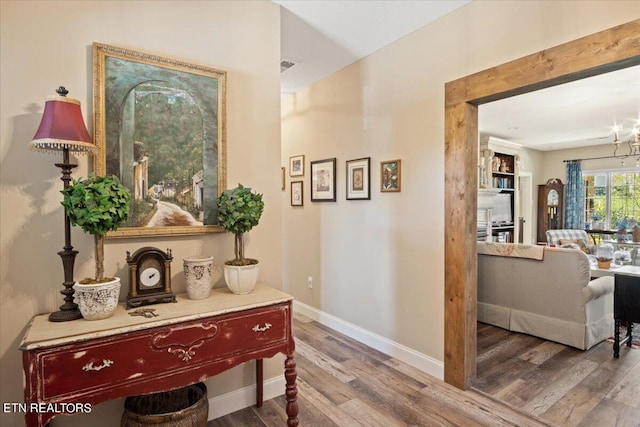 hallway featuring wood-type flooring and an inviting chandelier