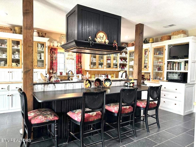 kitchen with white cabinetry, sink, dark tile patterned flooring, a kitchen breakfast bar, and a textured ceiling