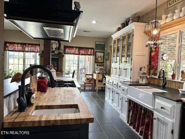 kitchen featuring butcher block countertops, dark tile patterned flooring, sink, and white cabinets