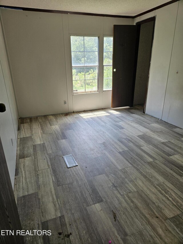 unfurnished bedroom with a textured ceiling, wood finished floors, and ornamental molding
