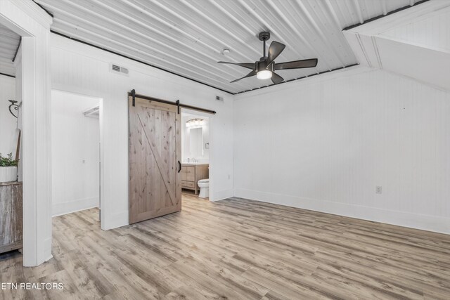 unfurnished bedroom featuring light hardwood / wood-style flooring, connected bathroom, a barn door, a spacious closet, and a closet