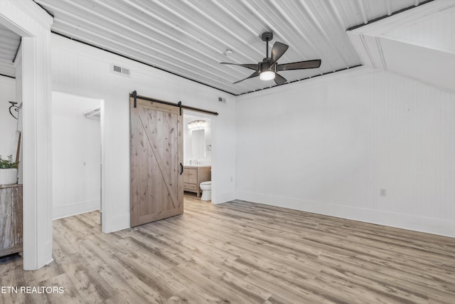 unfurnished bedroom with wood finished floors, visible vents, ensuite bath, a spacious closet, and a barn door