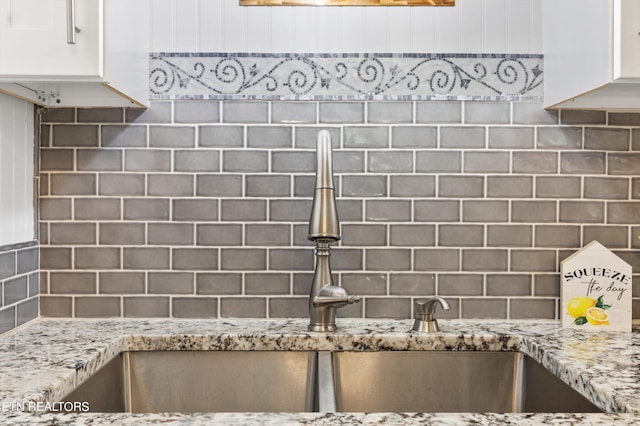 interior details featuring sink, decorative backsplash, light stone countertops, and white cabinets