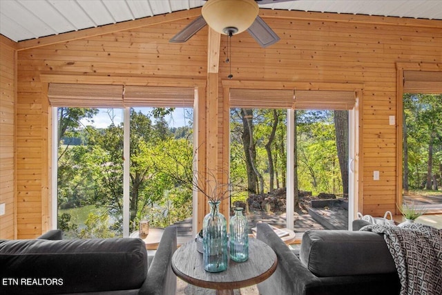 living area featuring lofted ceiling, wood walls, and a ceiling fan