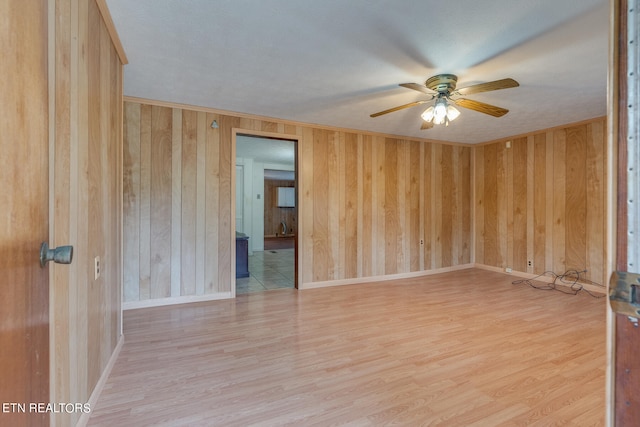 empty room featuring light hardwood / wood-style flooring, a textured ceiling, ceiling fan, and wooden walls