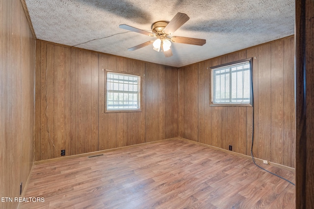 unfurnished room with wood walls, a textured ceiling, ceiling fan, and wood-type flooring