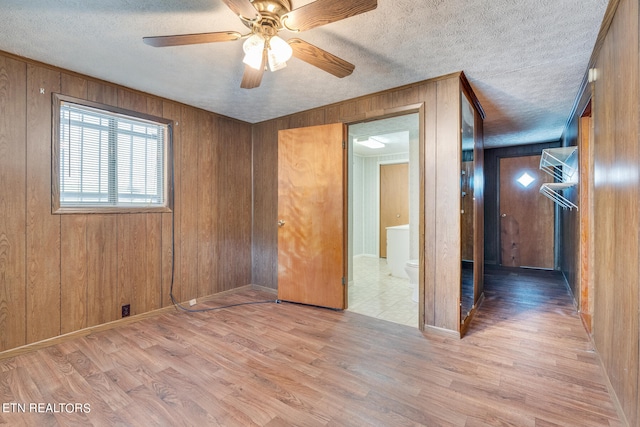 empty room with wood walls, wood-type flooring, ceiling fan, and a textured ceiling