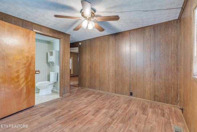 unfurnished bedroom featuring ensuite bath, wood walls, and light hardwood / wood-style floors