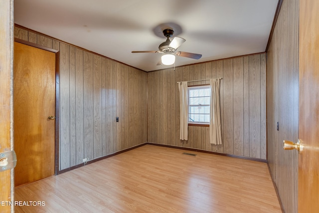 unfurnished room featuring wooden walls, light wood-type flooring, ceiling fan, and ornamental molding