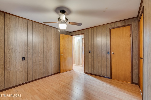 unfurnished bedroom featuring a closet, light hardwood / wood-style floors, wooden walls, and ceiling fan