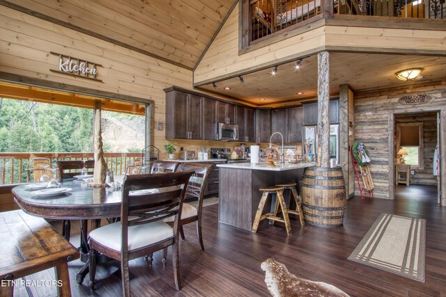 dining area with wooden walls, dark wood-type flooring, wooden ceiling, sink, and high vaulted ceiling