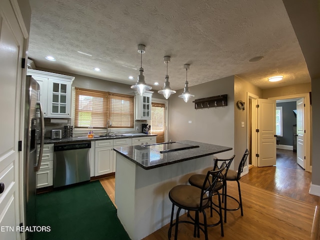 kitchen with stainless steel appliances, a center island, light hardwood / wood-style floors, white cabinets, and decorative light fixtures