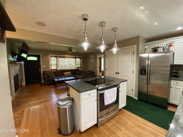 kitchen with pendant lighting, wood-type flooring, white cabinets, stainless steel appliances, and a brick fireplace