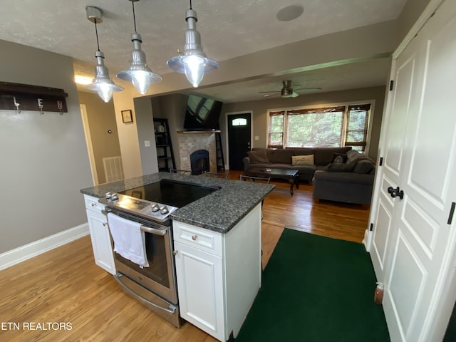 kitchen with stainless steel electric stove, decorative light fixtures, white cabinetry, dark stone counters, and light hardwood / wood-style floors